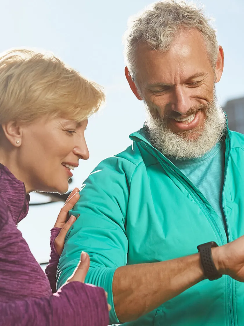 An older couple outdoors checking a smartwatch together
